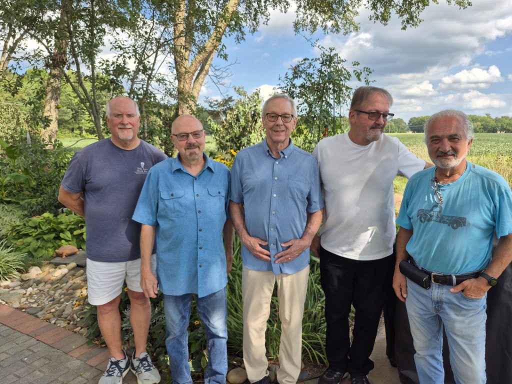 The five members of REUNION Band outdoors, with Delaware farmland behind them